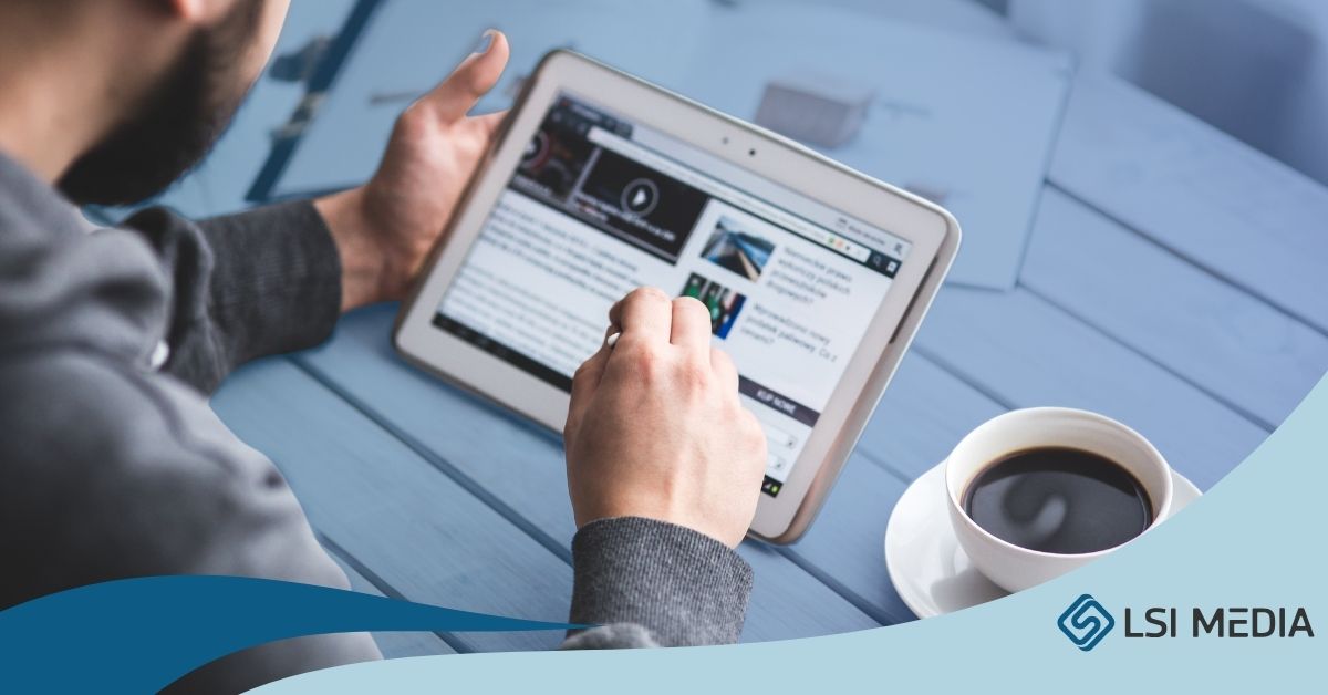 The image shows a person holding a tablet and browsing a website, with one hand touching the screen. A cup of coffee sits on the table nearby, creating a relaxed and casual setting.